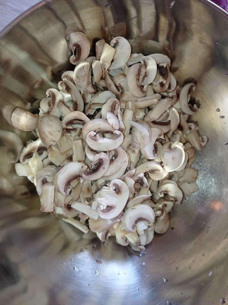 Freshly chopped mushrooms arranged in a stainless steel bowl, showcasing their natural textures