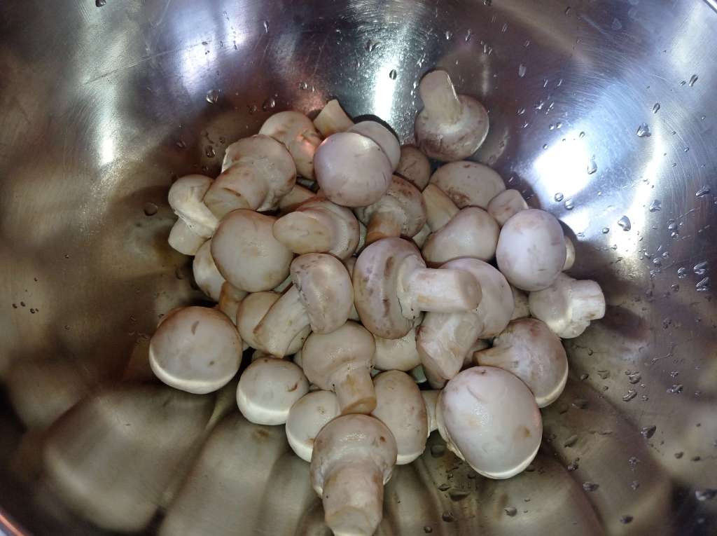 A stainless steel bowl filled with freshly washed mushrooms, showcasing their natural textures