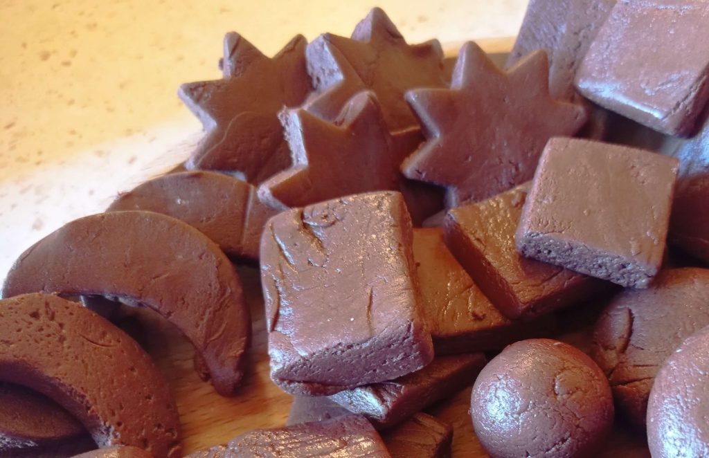 A wooden plate filled with homemade chocolate fudge in various shapes, showcasing its rich texture and deep brown color