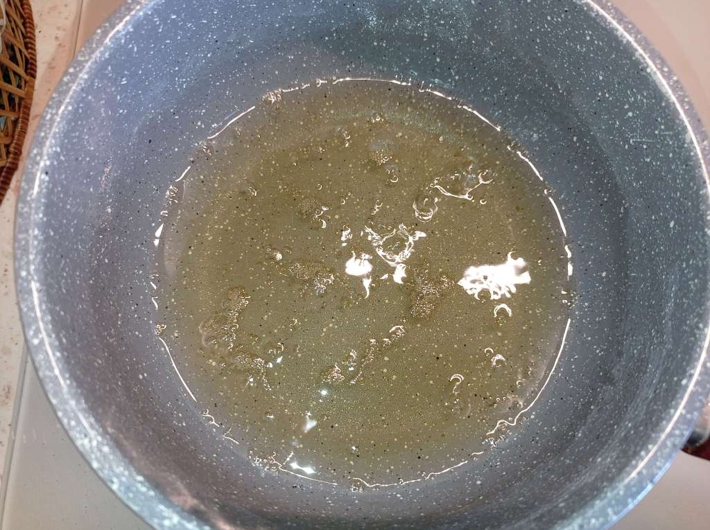 A bubbling sugar syrup mixture of water, sugar, vanilla, and orange extract cooking on the stove for homemade chocolate fudge.