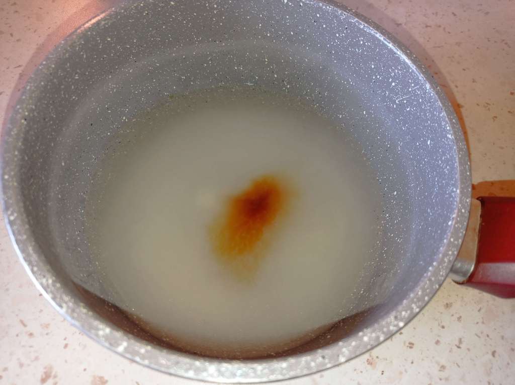 Small saucepan on the stove with sugar, water, vanilla extract, and orange extract for homemade chocolate fudge.