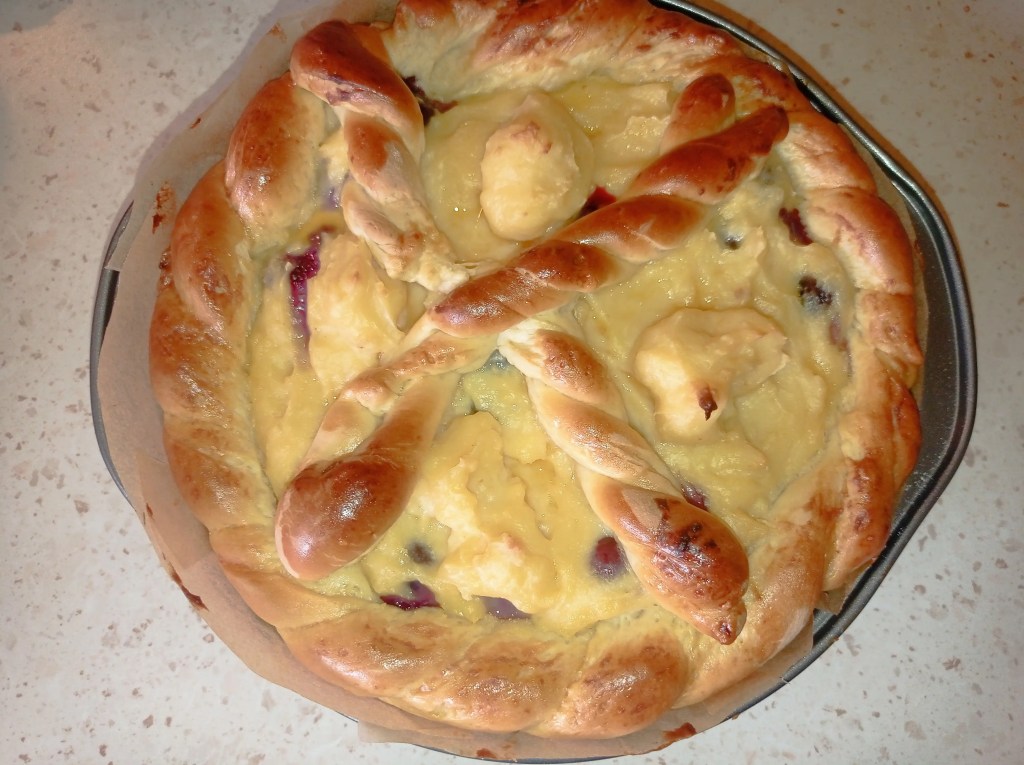 Top view of a baked dairy-free Romanian Pasca with twisted dough cross, golden crust, and creamy vanilla filling with visible blueberry spots