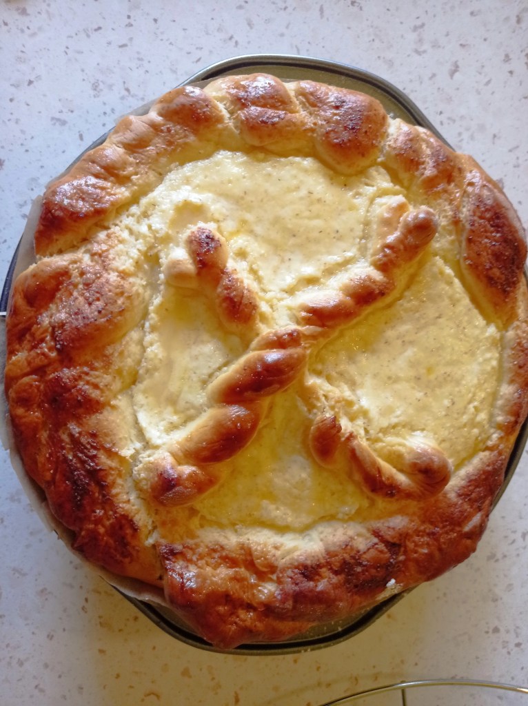 Top view of golden-brown Romanian Pasca with braided crust and dough cross, freshly baked in round pan
