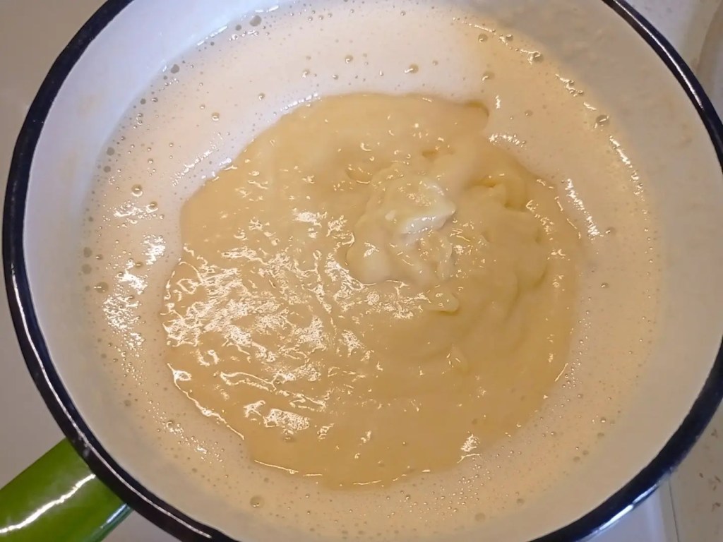 Custard mixture bubbling gently at the center, forming a light foamy ring as it begins to boil