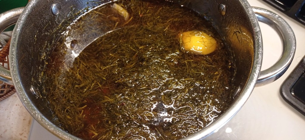 Deep reddish-brown fir syrup bubbling in a pot, with lemon peel visible, ready to be strained and bottled