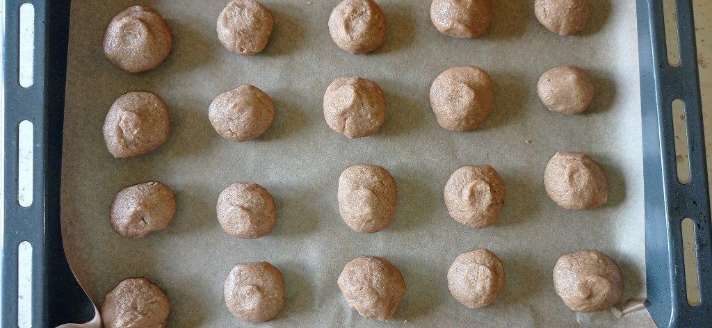Unbaked halva cookies shaped into balls, placed on a parchment-lined baking tray