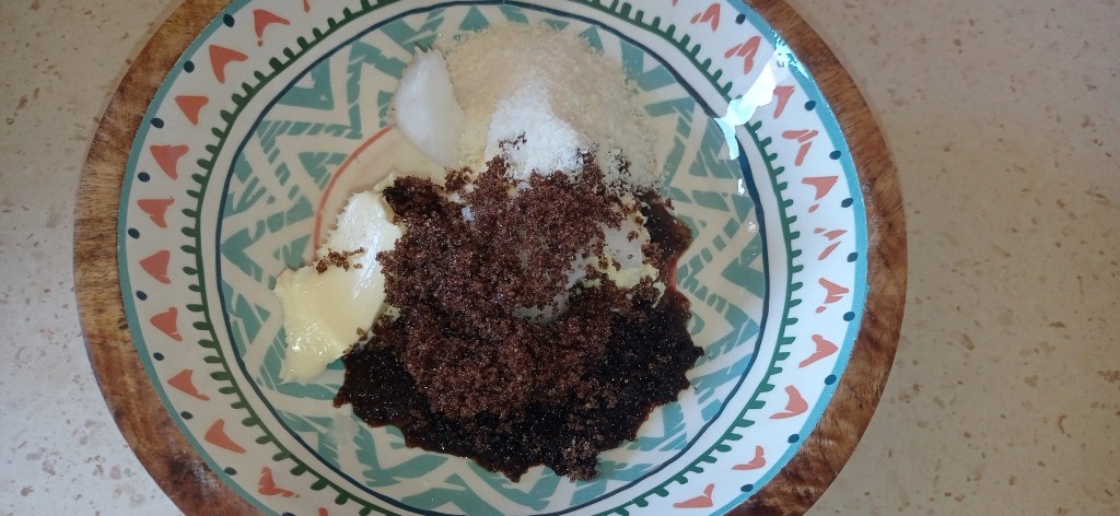 Coconut oil, cocoa halva, shredded coconut and sugar in a colorful ceramic bowl