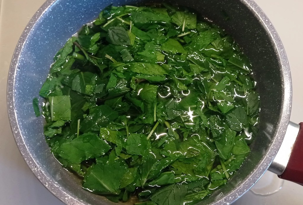 A pot filled with freshly chopped mint leaves steeping in hot water, preparing a natural infusion for syrup