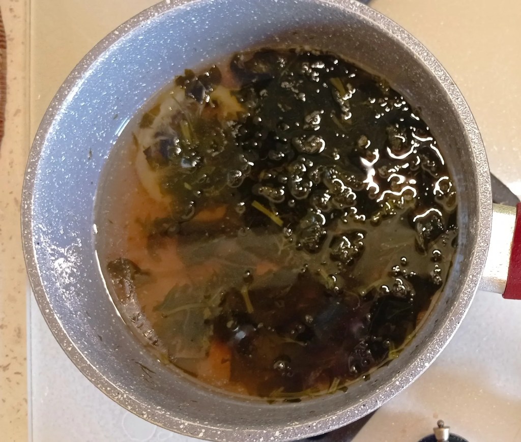 A pot of mint syrup simmering on the stove, with visible mint leaves and lemon slices floating in the liquid
