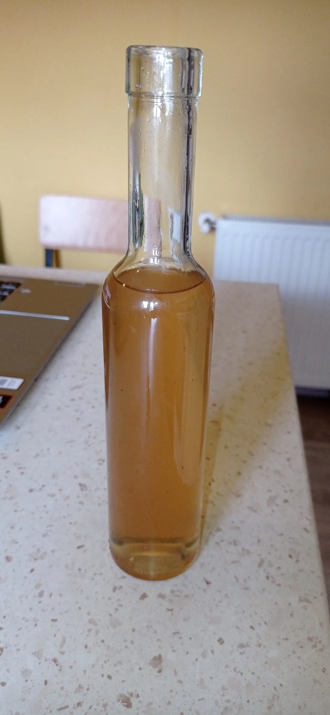 A clear glass bottle filled with freshly made mint syrup, warm and golden-brown in color