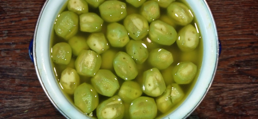 Peeled green walnuts with visible piercings soaking in water, beginning to release color