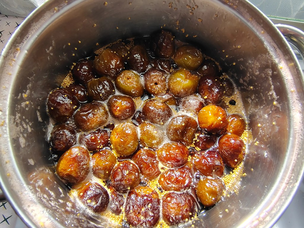 Whole figs resting in thickened syrup after the first 10 minutes of boiling, during the fig jam cooking process.