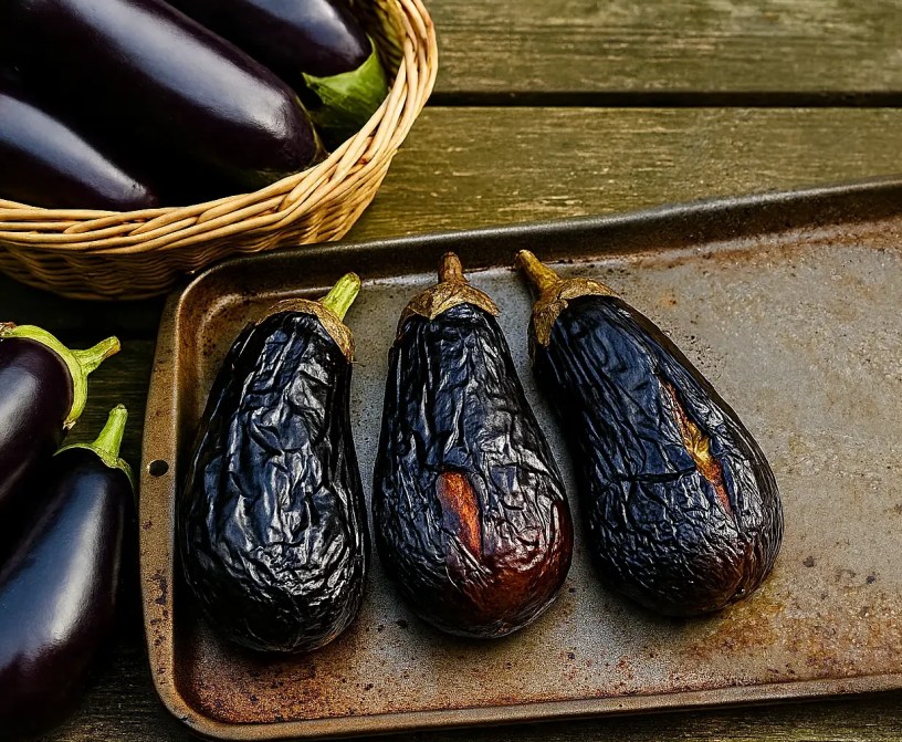 Whole roasted eggplants arranged on a tray, cooling and ready to be prepared for freezing