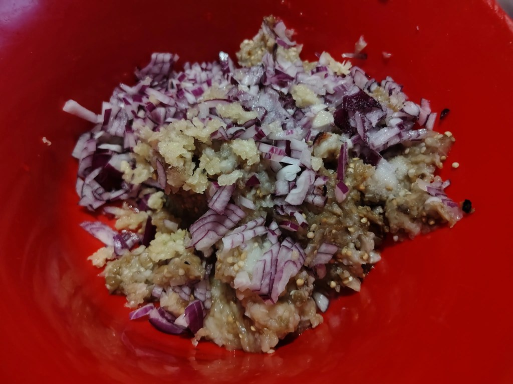 chopped roasted eggplant mixed with finely diced red onion and garlic in a red bowl