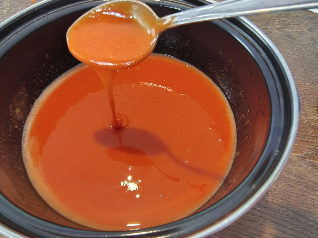 Rosehip paste diluted with sugar and lemon, shown in a bowl with a spoon, ready to be cooked into a thick spread.