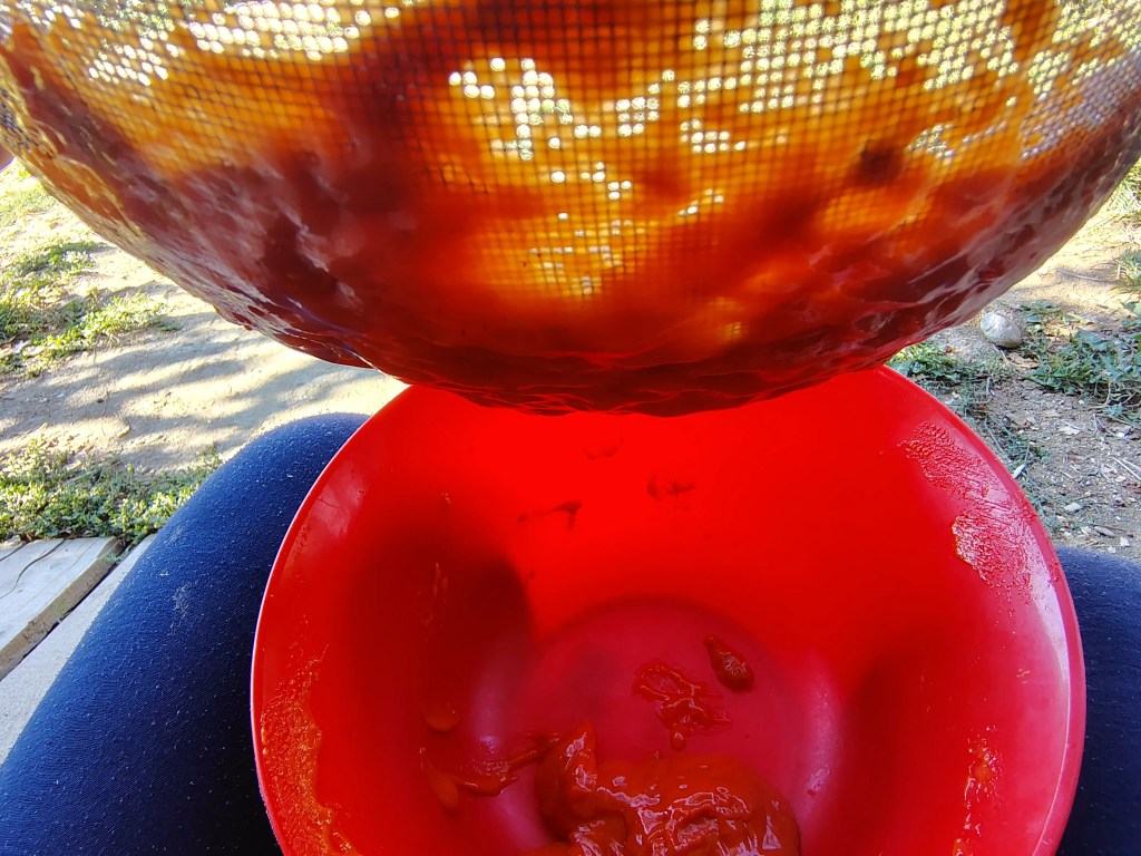 Smooth rosehip purée dripping through the sieve into a bowl during straining.